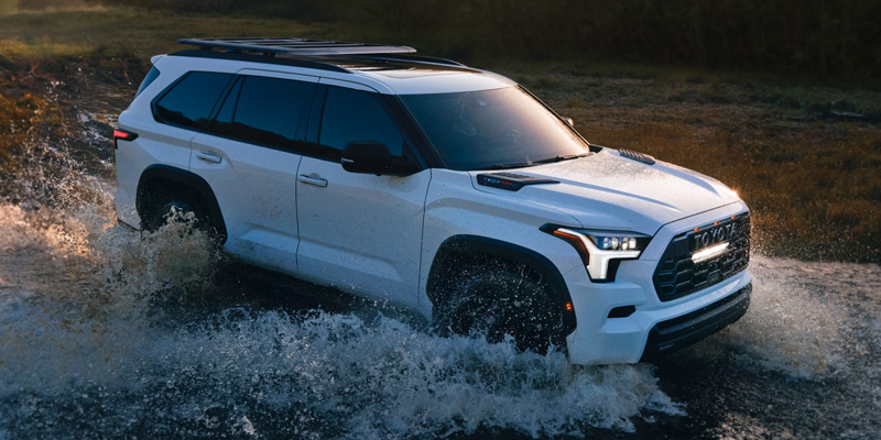 A white 2025 Toyota Sequoia TRD Pro driving through water, creating large splashes.
