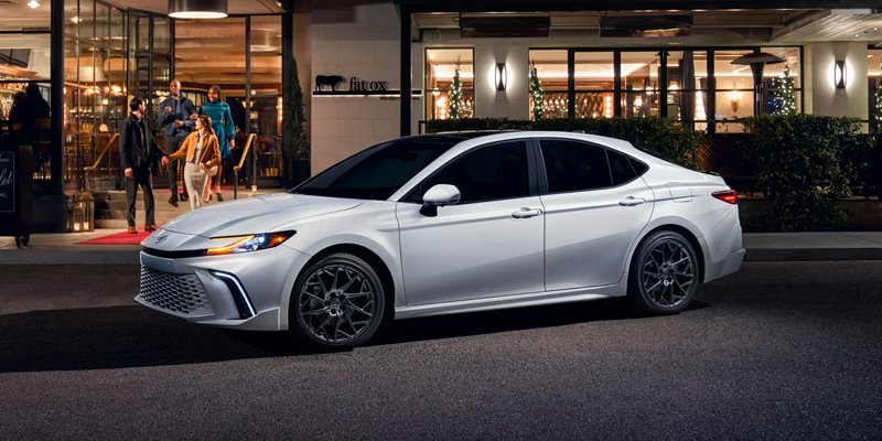 A white 2025 Toyota Camry parked in front of a restaurant