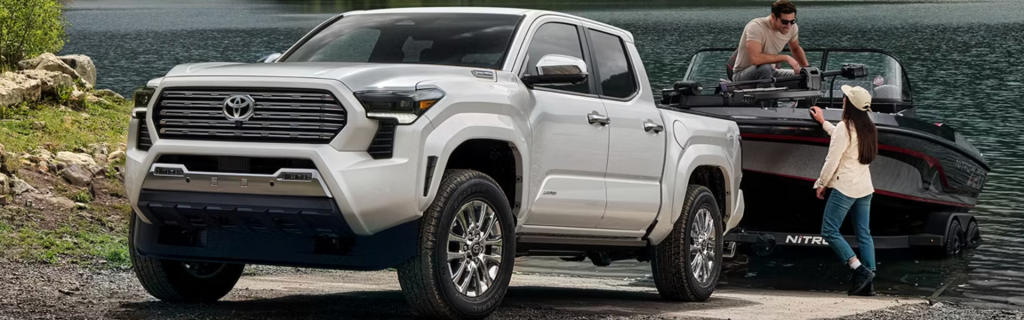 Toyota Tacoma truck towing a boat at a lakeside, highlighting strong towing capacity, off-road capability, Toyota Safety Sense features, and versatile outdoor performance.