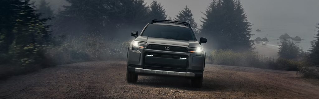 Toyota RAV4 Plug-in Hybrid driving on a foggy forest road near the coastline with headlights on, showcasing rugged hybrid performance and adventure-ready capability.