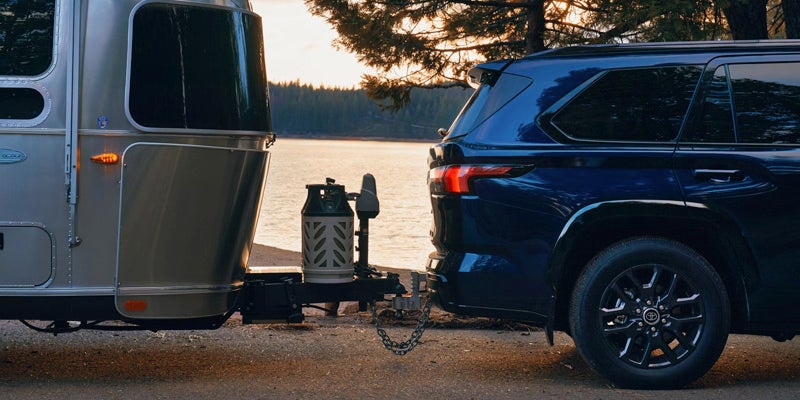 Blue Toyota SUV towing a travel trailer beside a lake at sunset.